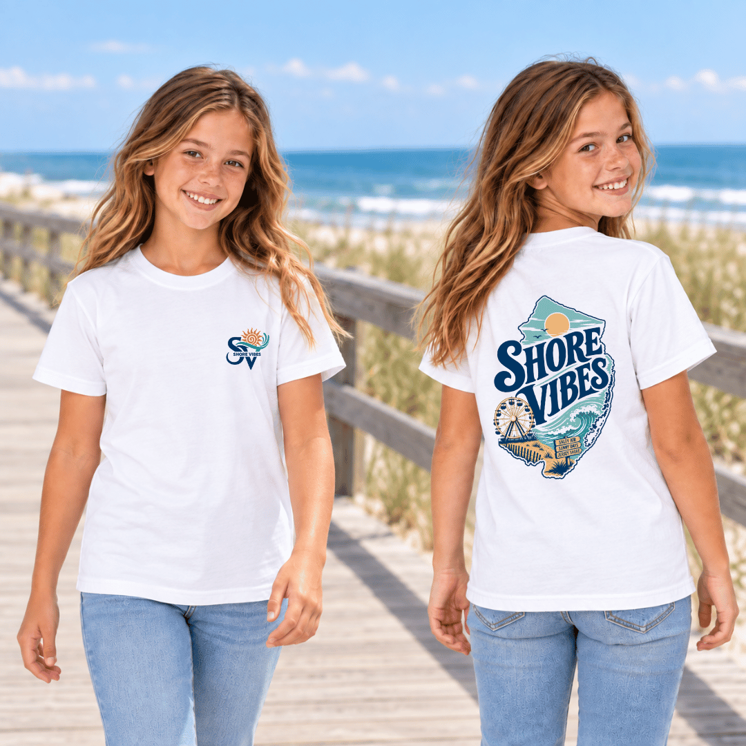 A girl in white Shore Vibes t-shirts on a boardwalk, one showing the front logo and one showing the back graphic