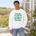 A man wearing a white crewneck sweatshirt with a green 'We're All A Little Irish Today' graphic, standing outdoors in front of a house and dunes.