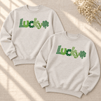 Two Heather Dust crewneck sweatshirts laid flat, showing green Lucky lettering and plaid shamrocks