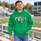 Man in jeans walking in a stadium, wearing a Kelly green Philly pullover hoodie with white varsity PHILLY lettering and an eagle carrying a football on the chest
