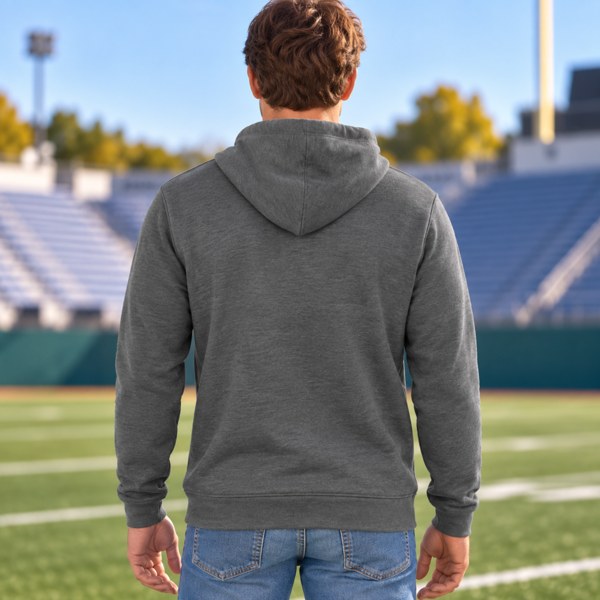 Back view of a man wearing a plain Deep Heather Bella & Canvas hoodie at a football stadium