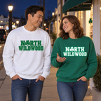 Man in a white North Wildwood sweatshirt and woman in a Kelly Green version walking together outdoors at night