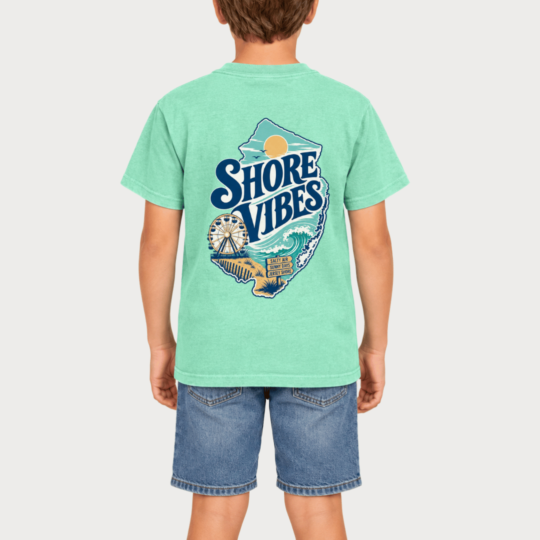 Back view of a boy in an Island Reef green Shore Vibes t-shirt showing the full New Jersey coastal graphic, studio photo