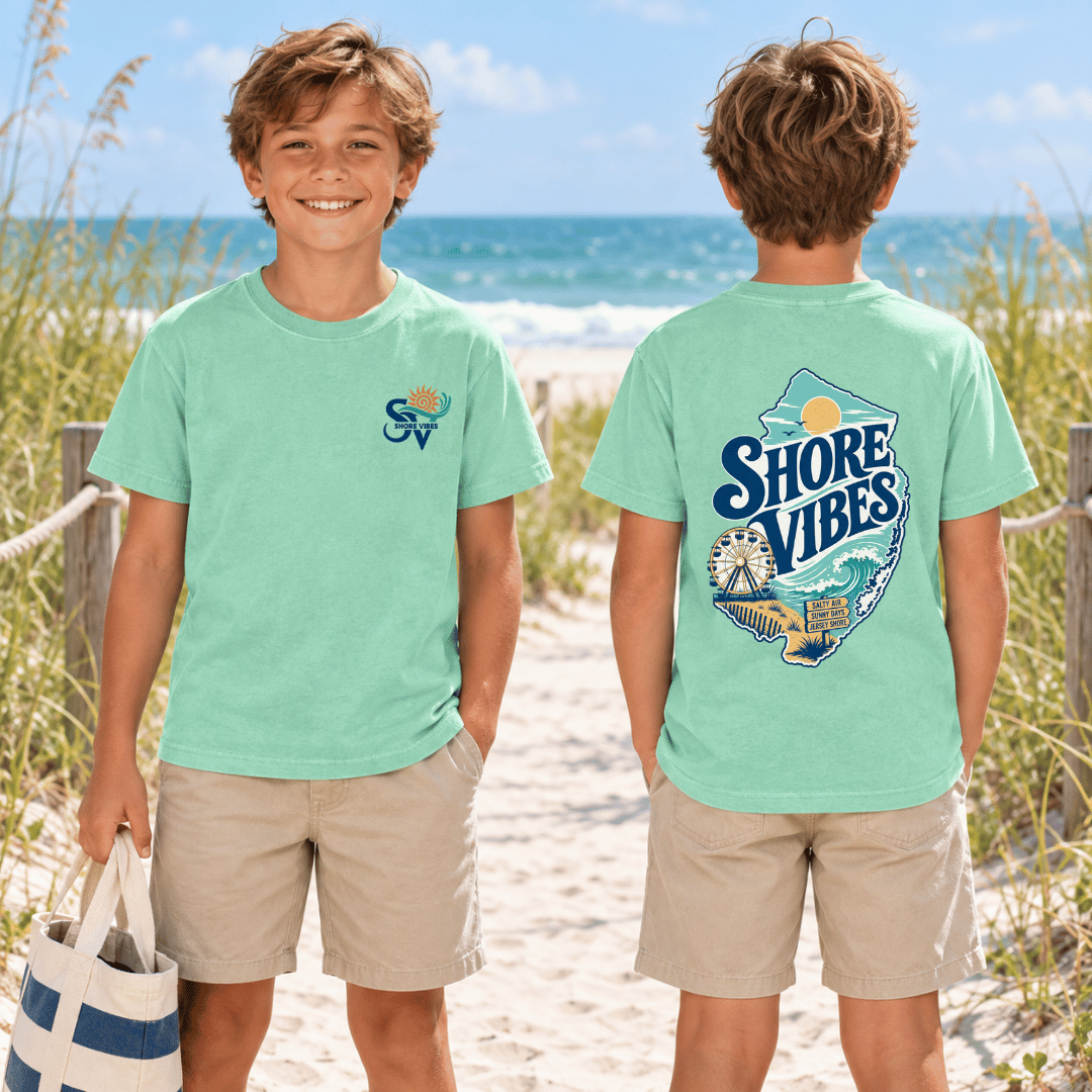 A boy in Island Reef green Shore Vibes t-shirts on a beach path, one showing the front logo and one showing the back graphic