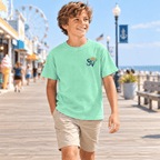Boy wearing an Island Reef green Shore Vibes t-shirt with the front logo, walking a boardwalk near a beach ferris wheel