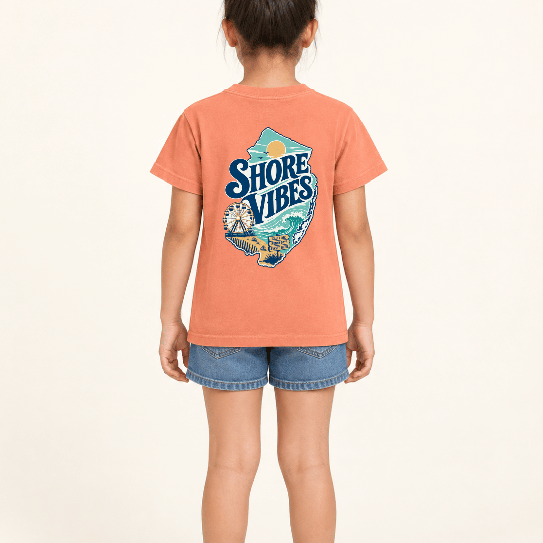 Back view of a girl in a Melon orange Shore Vibes t-shirt showing the full New Jersey coastal graphic, studio photo