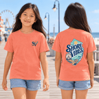 Girl wearing a Melon orange Shore Vibes t-shirt with the front logo on a boardwalk path near the beach