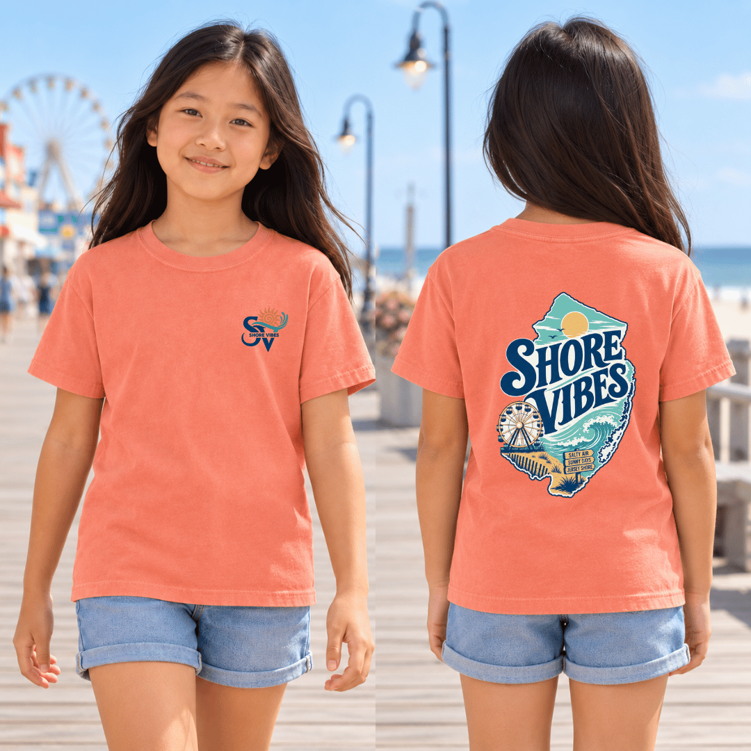 Girl wearing a Melon orange Shore Vibes t-shirt with the front logo on a boardwalk path near the beach