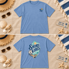 Washed denim Shore Vibes t-shirt flat lay showing the front logo and full back graphic on a beach themed background