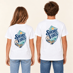 Two children shown from the back wearing matching white graphic T-shirts with a large 'Shore Vibes' logo, paired with blue jeans against a plain light beige background.