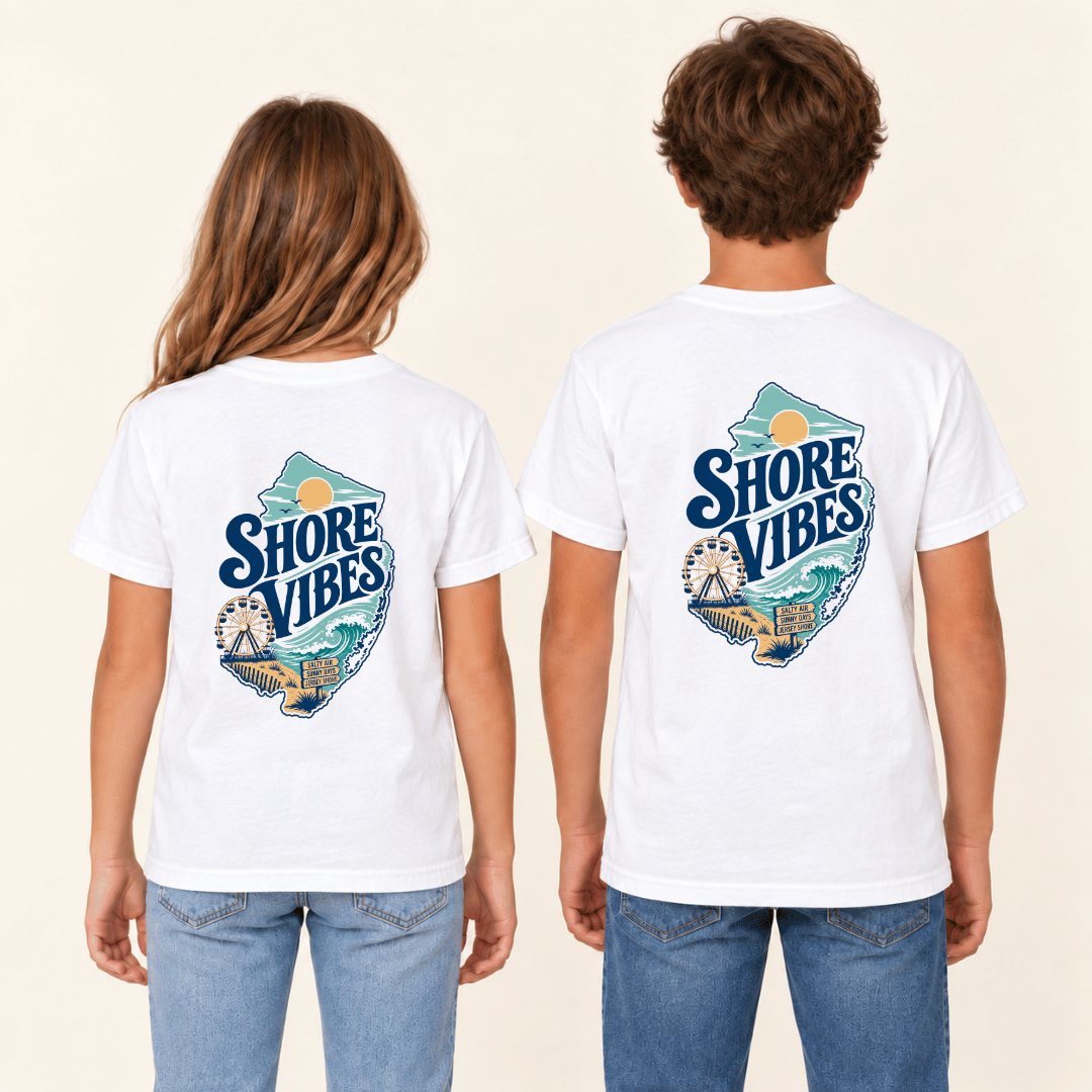 Two children shown from the back wearing matching white graphic T-shirts with a large 'Shore Vibes' logo, paired with blue jeans against a plain light beige background.