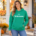 Smiling woman on a fall front porch wearing a Kelly Green 'tis the season football hoodie and jeans