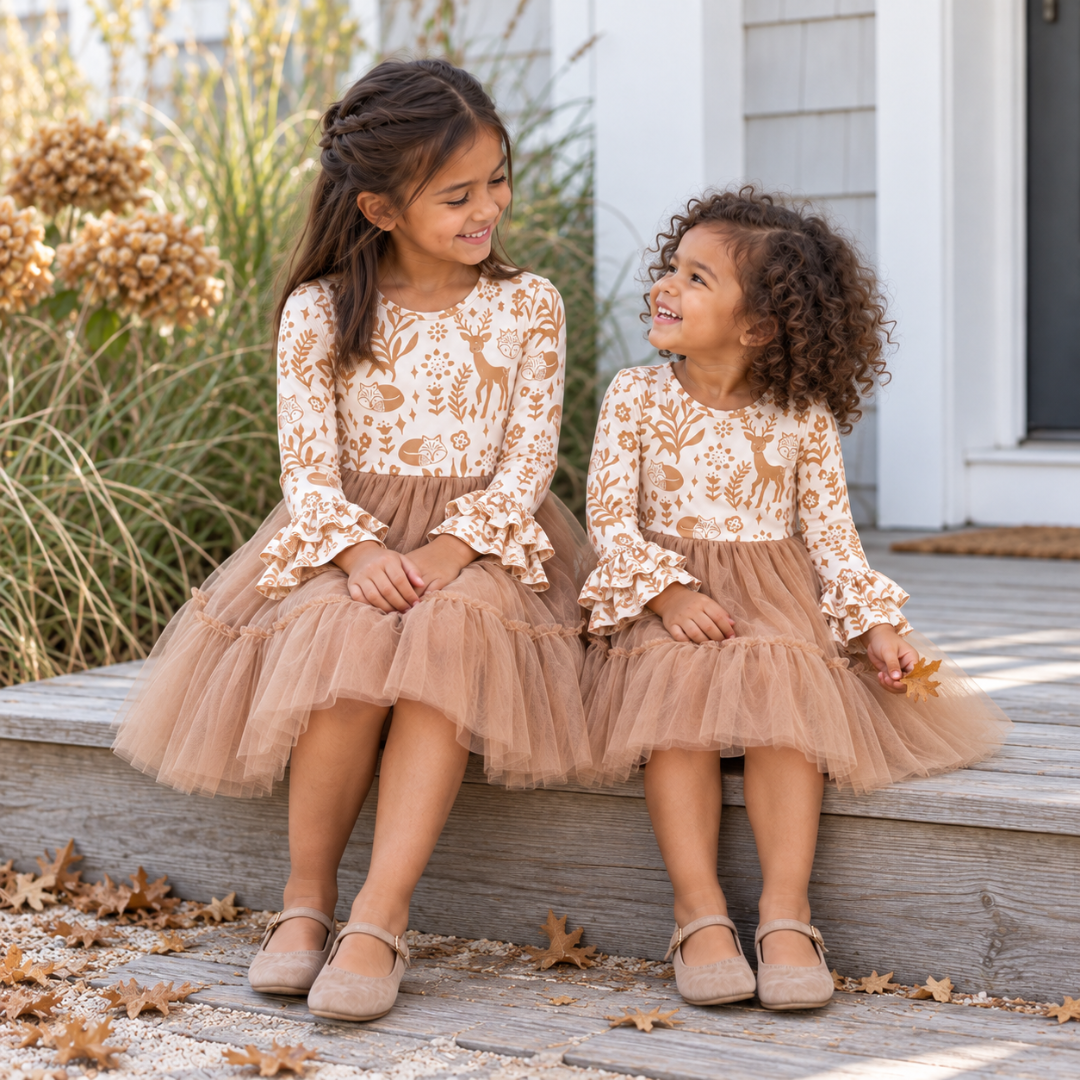 Two children sitting on porch steps in matching woodland deer dresses with tan tulle skirts