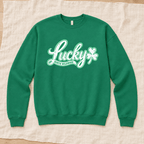 A kelly green crewneck sweatshirt with a white graphic reading 'Lucky North Wildwood' and a shamrock, laid flat on a beige linen fabric background.