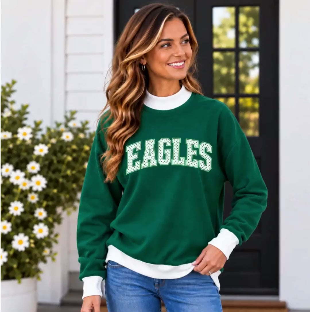 Woman wearing a dark green sweatshirt with white contrast collar, cuffs and hem, and white polka dot "EAGLES" varsity lettering across the chest