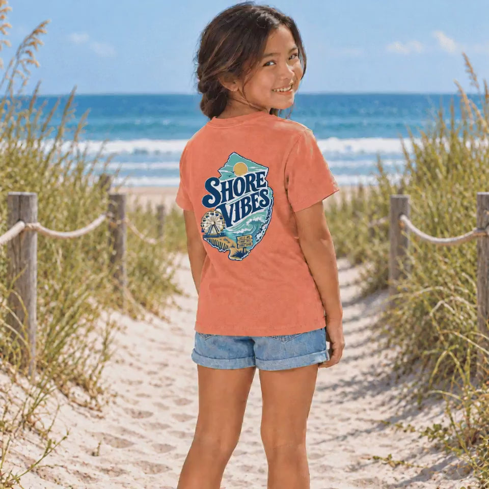 Front and back view of a girl in a Melon orange Shore Vibes t-shirt walking a boardwalk path toward the beach