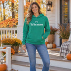 Video of a smiling woman wearing a Kelly Green 'tis the season football hoodie and jeans on a fall front porch with mums and pumpkins