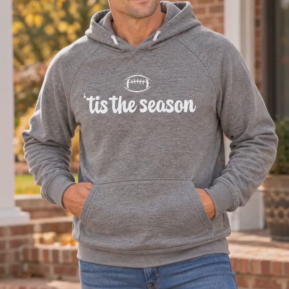 Video of a man wearing a Deep Heather grey 'tis the season football hoodie with hands in the front pocket on a brick front porch